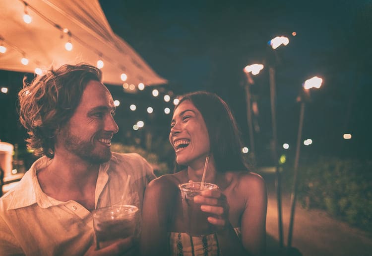 Couple laughing with drinks in their hands on a night out.