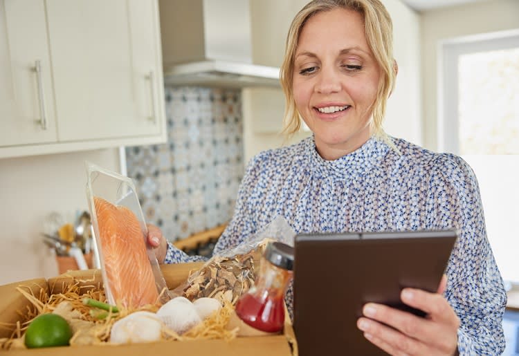 Woman holding a meal kit and looking at her tablet