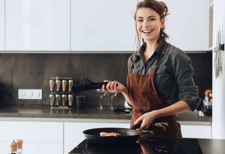 Smiling woman cooking fish in skillet