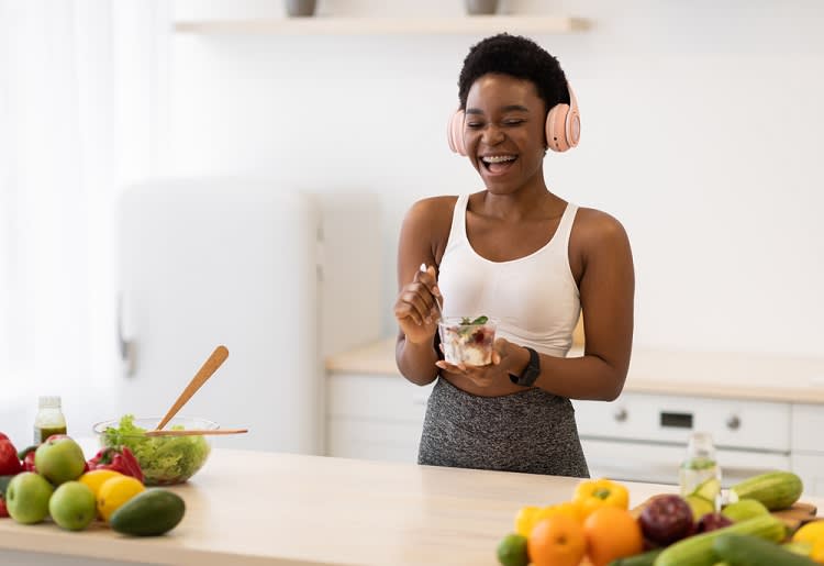 Woman in activewear and headphones eating breakfast in kitchen