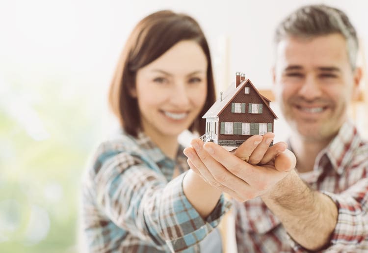 Couple holding a model house in their hands, while considering to buy a commercial appliance for their home.