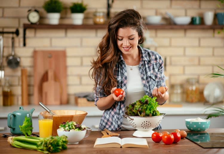 Woman making a salad and holding a tomato in one hand and egg in the other