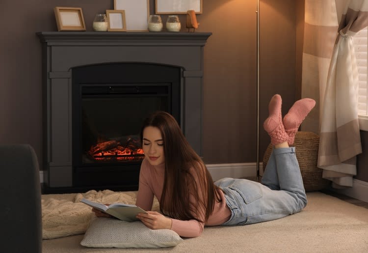Woman reading a book on the floor in front of fireplace