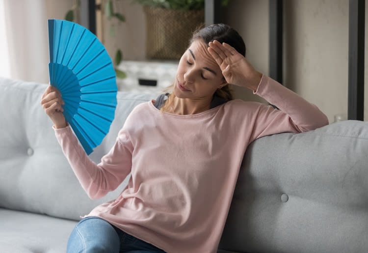 Woman holding fan and getting hot on couch