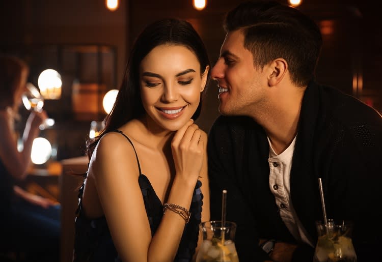 Man whispering in woman's ear at a bar