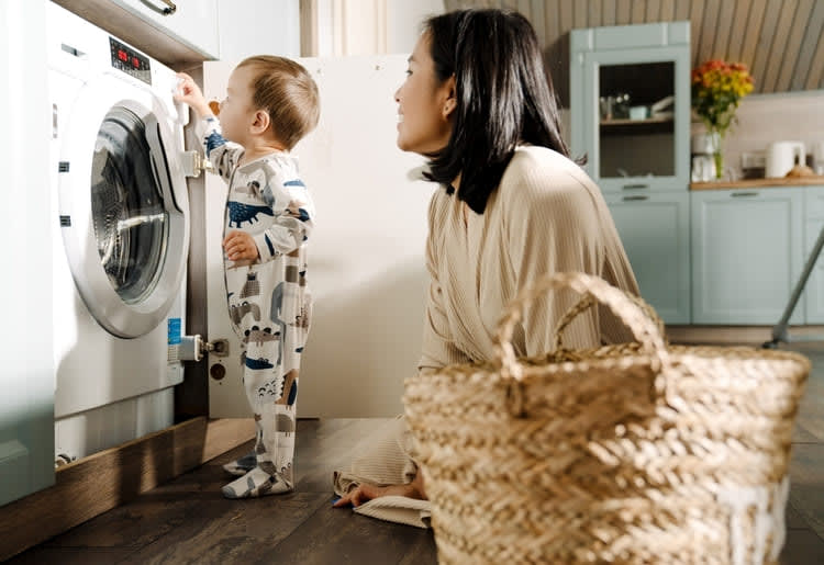 Child playing with washing machine controls while his mother watches him.