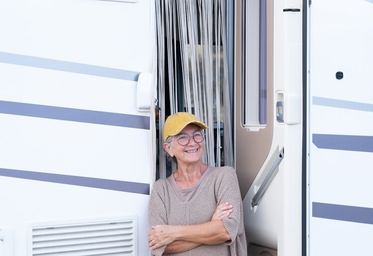 An elderly woman standing in front of a camper van, smiling with her arms cross in front of her chest.