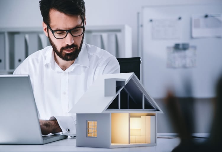 A man sitting at his laptop looking at a model of a house