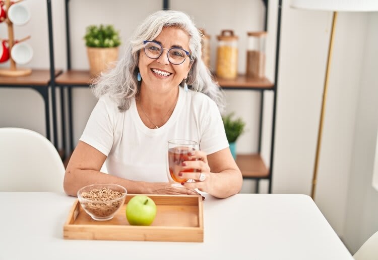 A mature woman smiling as she enjoys a balanced breakfast in her living room.