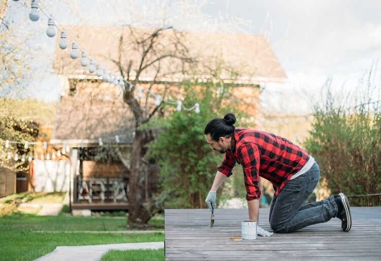 A middle-aged man varnishing the wooden deck in his back yard.