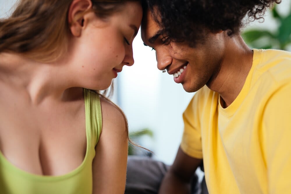 A couple sharing an intimate moment, both smiling with their foreheads resting together.