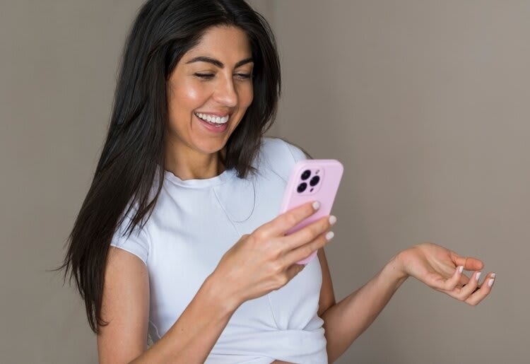 A young woman smiling widely at something on her phone.