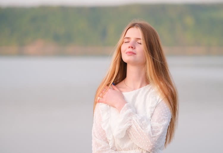 A woman with her eyes closed standing in front of a body of water