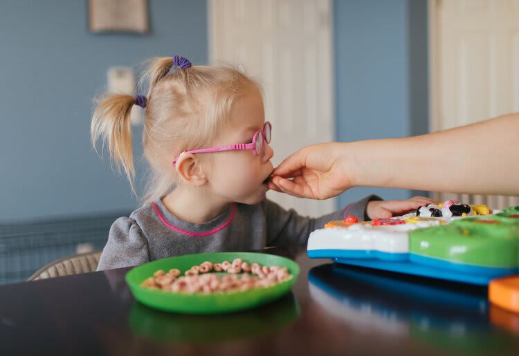 A small autistic girl being fed while she plays with a toy.