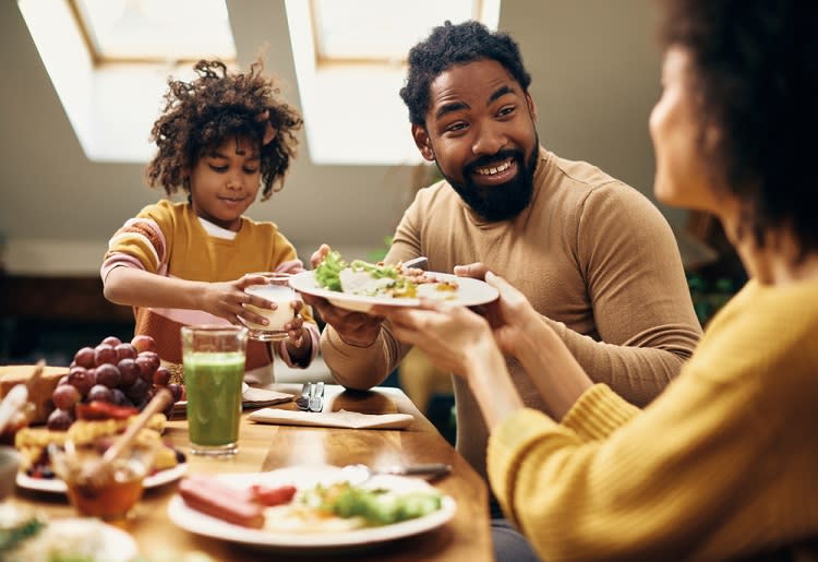 Mother passing plate of food to child and partner at dinner table