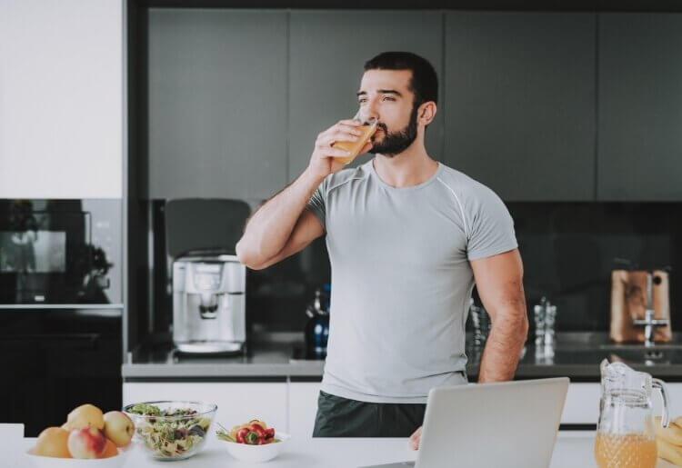 An athlete standing in a kitchen drinking healthy juice and prepping meals.