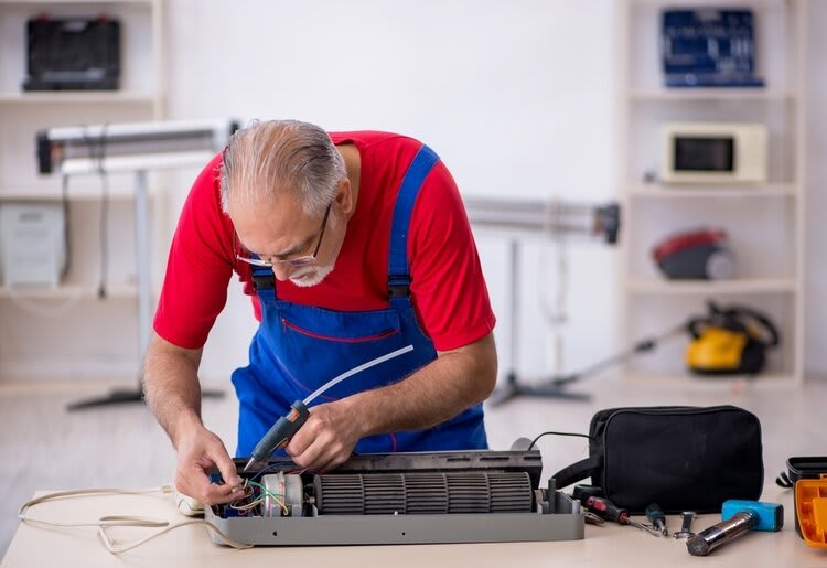An elderly technician busy fixing a broken AC compressor in his workshop.