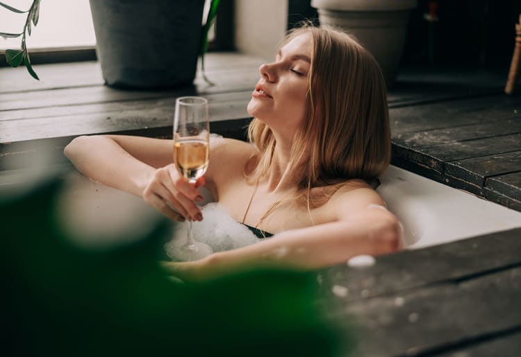 Woman relaxing in a bathtub, drinking champagne.