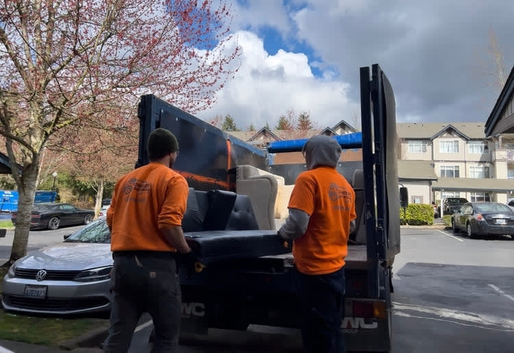 Two junk removal service men loading furniture onto a truck.