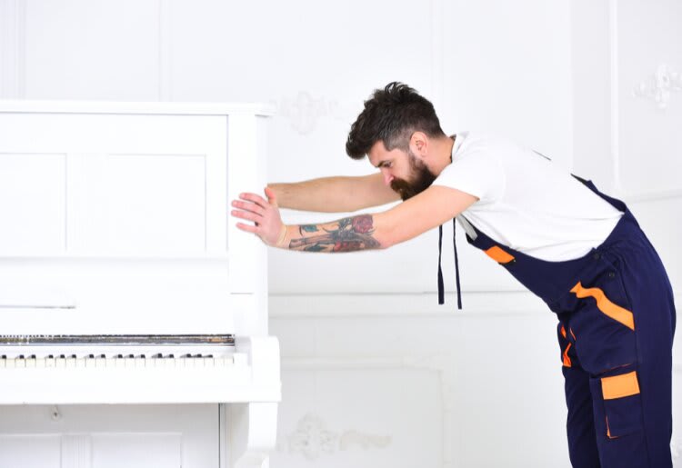 A man from a moving company moving a piano. 
