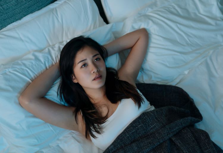 Young woman lying awake in bed at night.