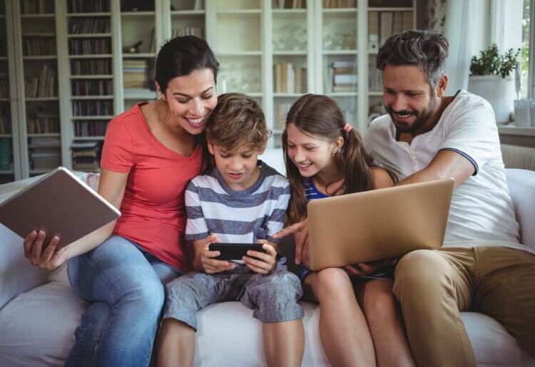A family sitting on a couch looking at mobile devices.