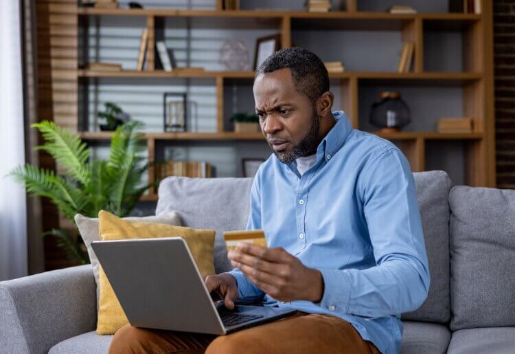 A man sitting on a couch looking at a laptop to try and figure out how to place a credit fraud alert.