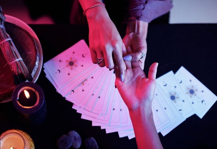 The hands of two people busy with a palm reading, with tarot cards and candles visible below.