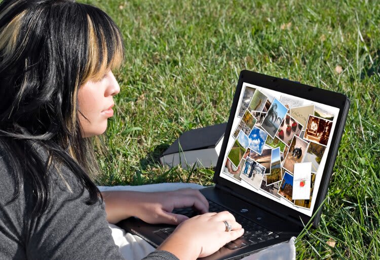 A woman sitting in the grass looking at a website gallery on her laptop.