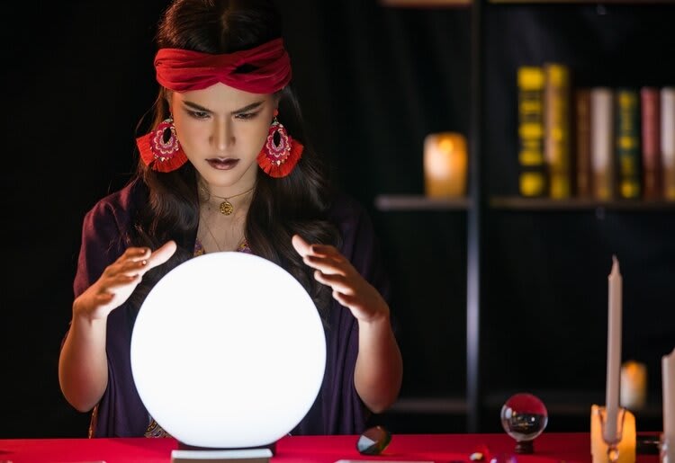 A medium seated in front of a glowing crystal ball.