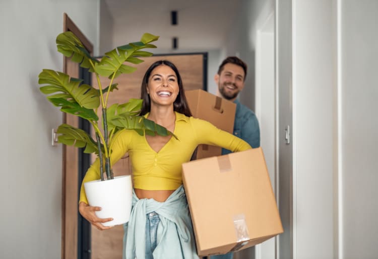 A man and woman carrying boxes and a plant.