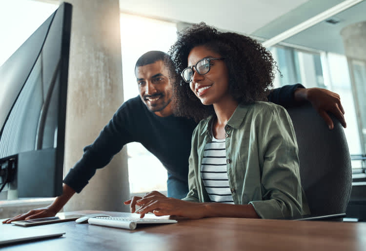 A man and a woman sitting at a desk in front of a computer.