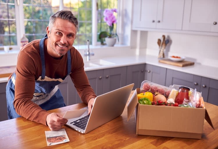 Smiling man holding a recipe card next to laptop and meal kit