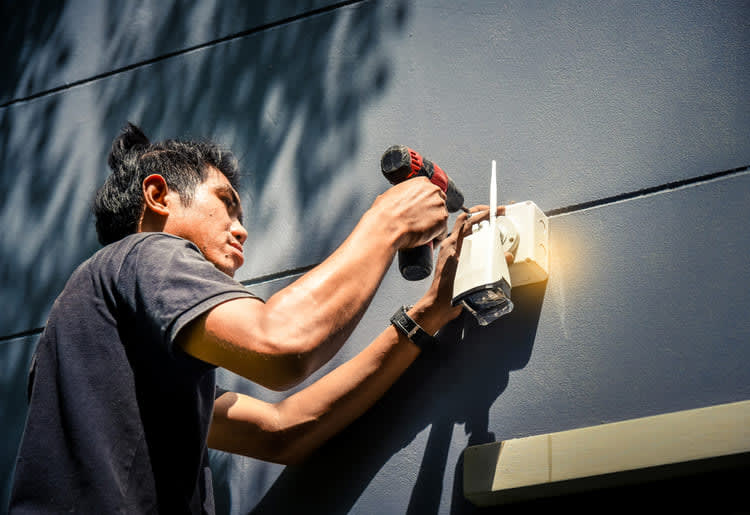 A man installing an outdoor wireless camera. 