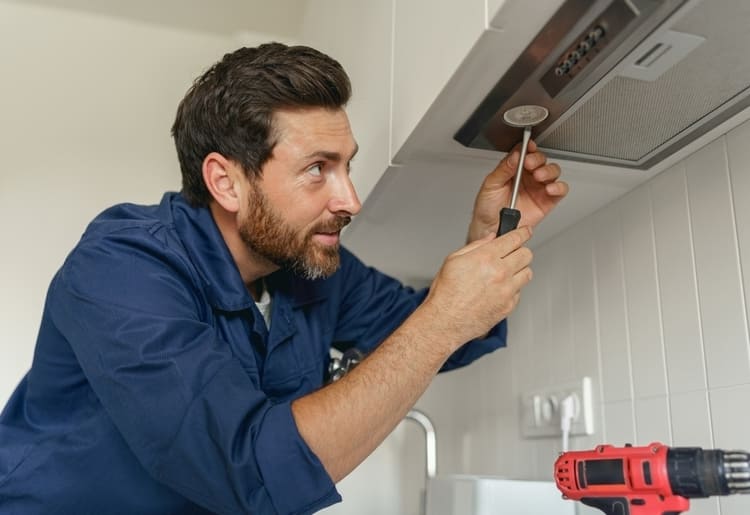 A home warranty technician fixing a stove in a kitchen.