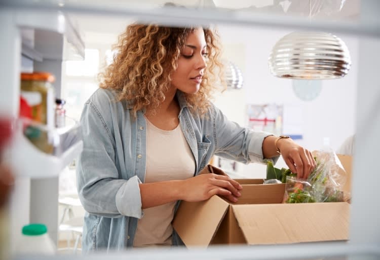 View from the refrigerator as a woman unpacks her meal kit delivery.