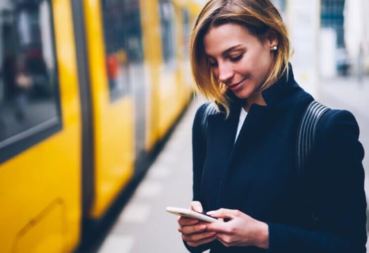 A woman standing next to a yellow train looking at her phone.