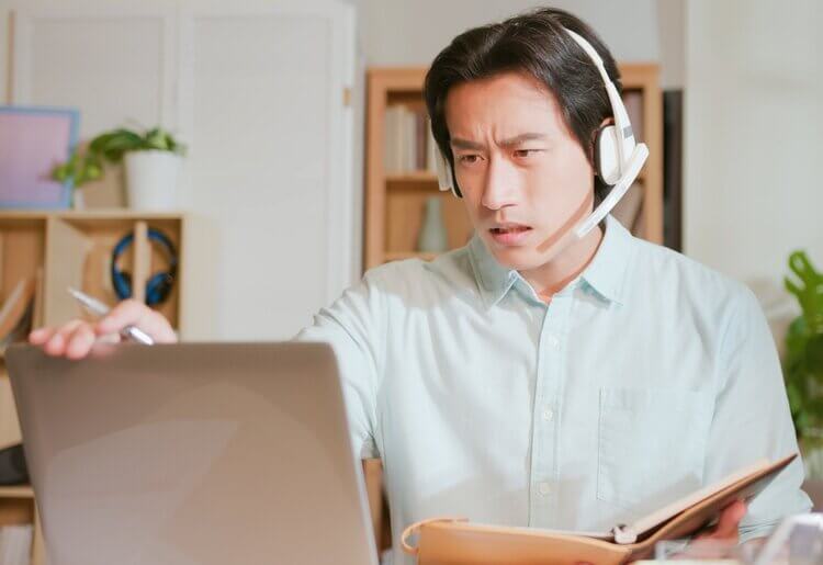 A man wearing a headset struggling to get good VoIP on his laptop during a video call.