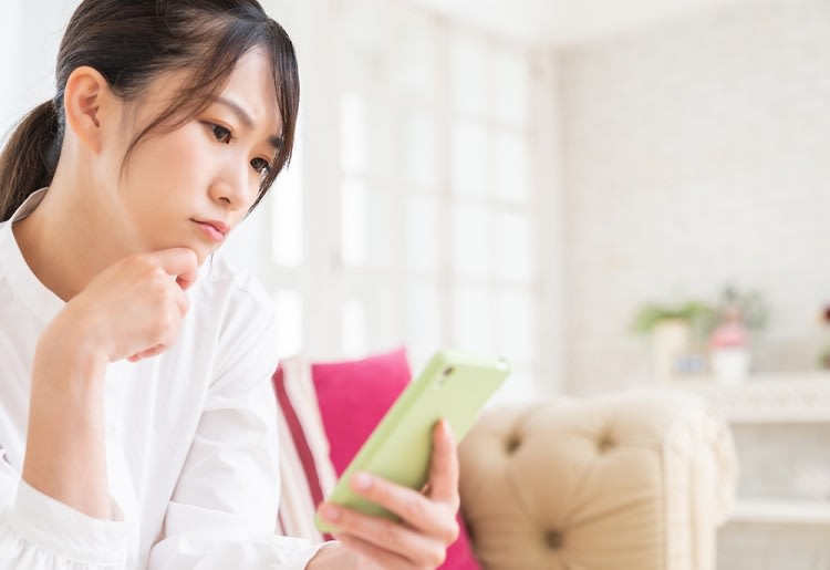 Woman sitting on couch looking at smartphone with contemplative look on her face