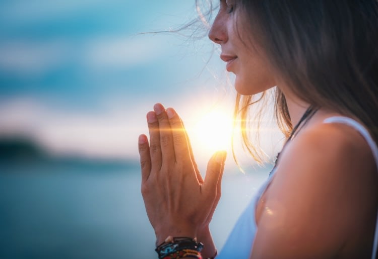 Woman meditating with her eyes closed, and her hands in prayer position.