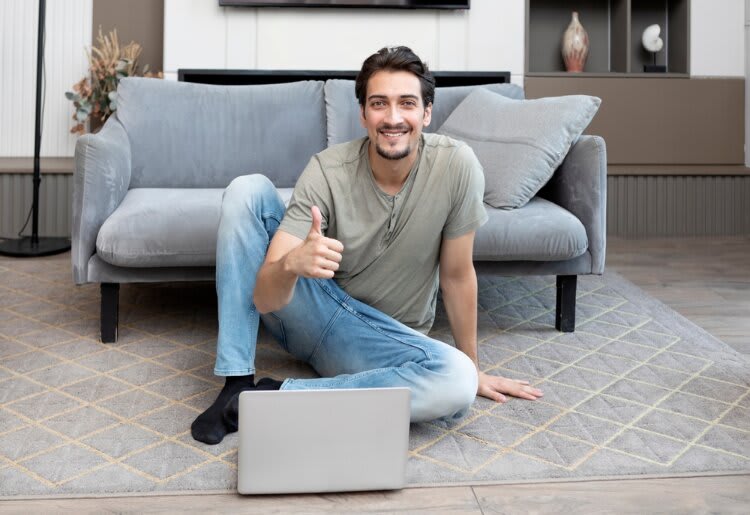 Smiling man giving a thumbs up in front of a laptop.