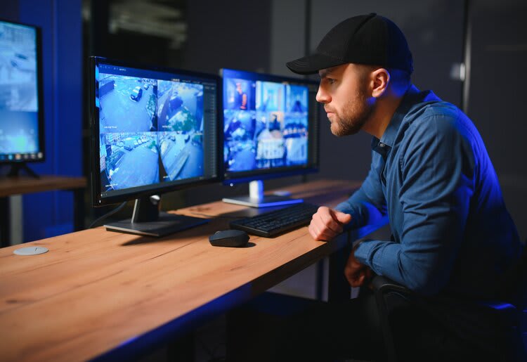 A man viewing home security camera footage on two computer monitors.