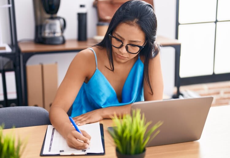 Woman doing paperwork in front of a laptop.