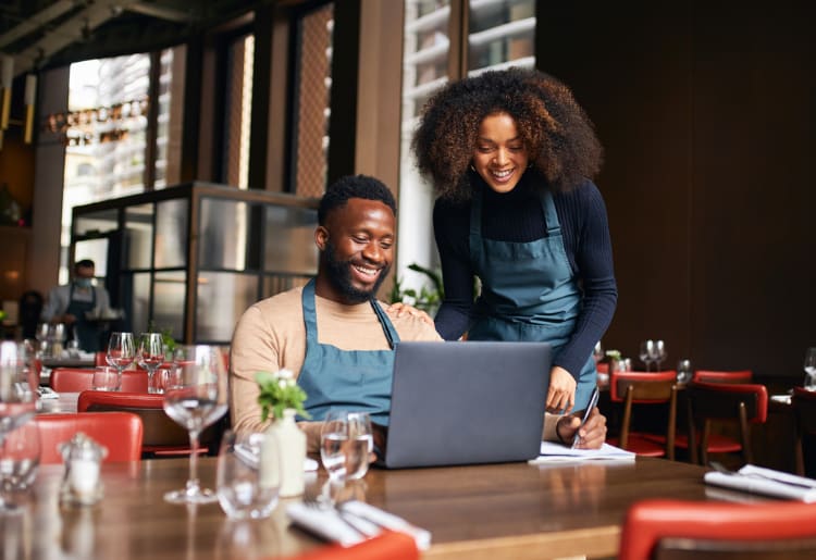 A man and woman sitting at a restaurant table with a laptop