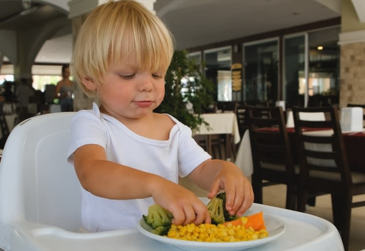Young child sitting in high chair playing with vegetables on a plate