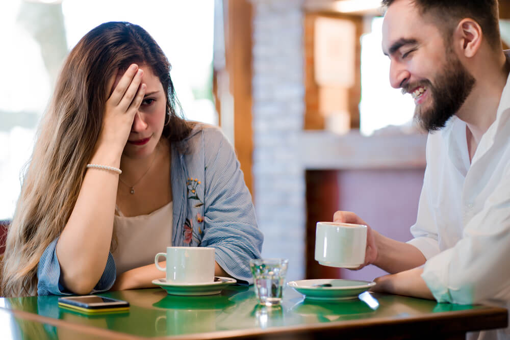 A woman on a date looking very bored while the man is laughing at something