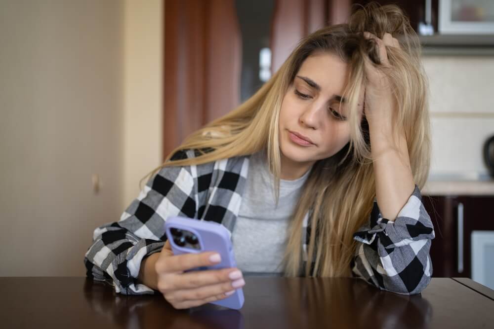 A girl sitting  looking perturbed while looking at her phone 
