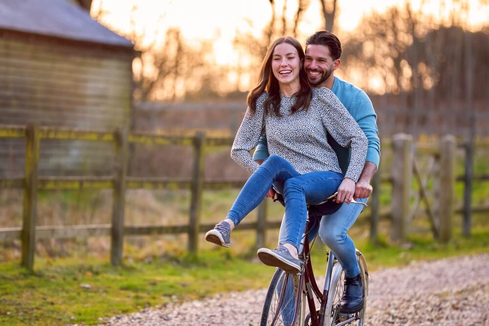 A couple riding a bike with  the girlfriend on the handles of the bike