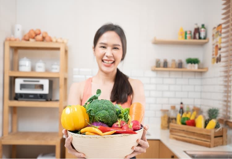 Smiling woman holding bowl of mixed fruits and vegetables