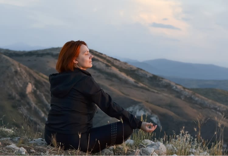 A woman sitting  on a mountaintop while meditating 